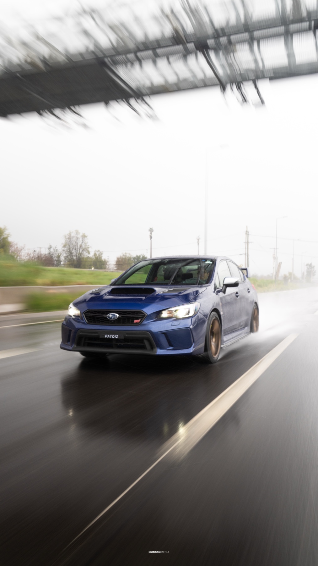 Subaru WRX STI en rolling shot bajo la lluvia, con reflejos en el pavimento